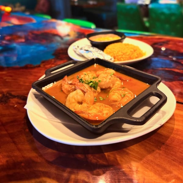 El Leoncito's shrimp dish in a black skillet with rice and beans on a wooden table.
