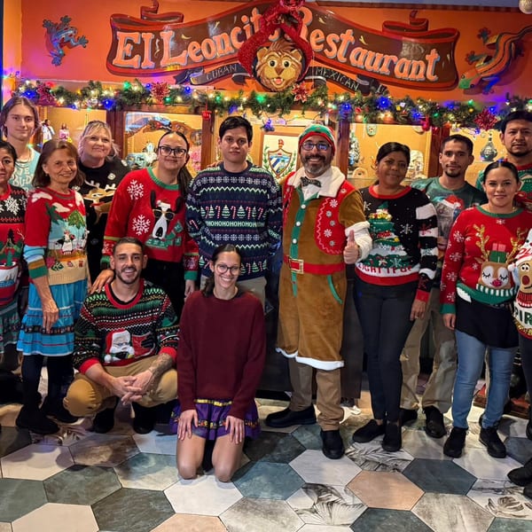 El Leoncito staff in festive Christmas sweaters pose in front of the restaurant's decorated sign.