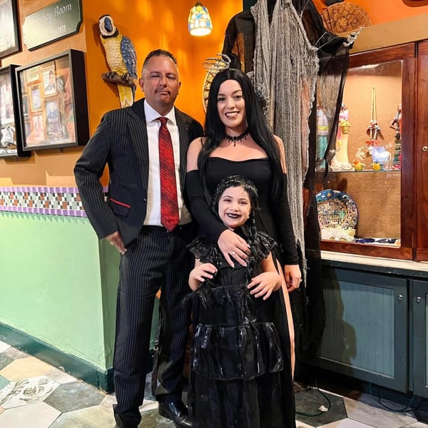 A family of three, dressed in black, posing in a restaurant decorated for Halloween.