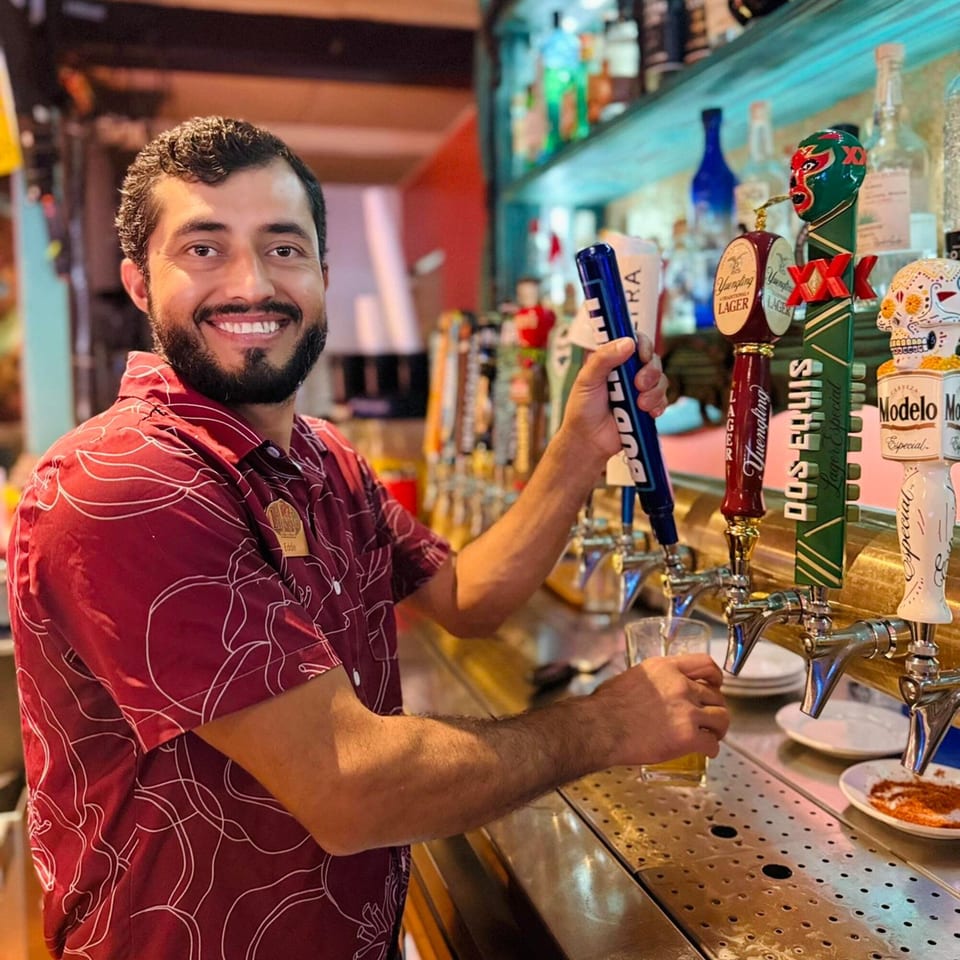 Smiling bartender Eddie pouring a beer from a tap at El Leoncito, a Mexican restaurant.