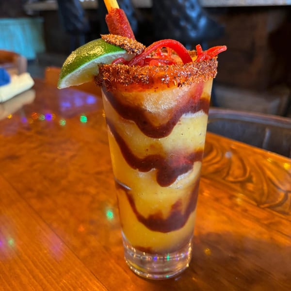 A vibrant mango chamoyada with chili powder rim, lime, and tamarind candy on a wooden table.