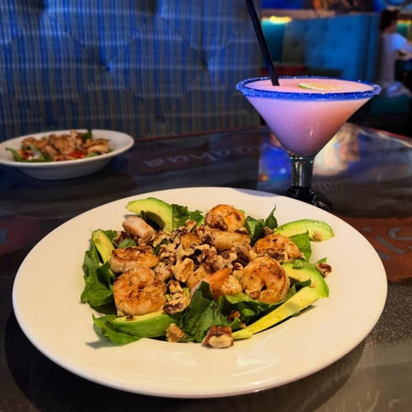 Shrimp and avocado salad with walnuts, alongside a pink margarita with a blue sugar rim.