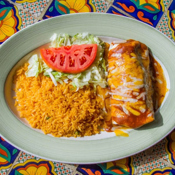A Mexican burrito with red sauce and melted cheese, served with rice, shredded lettuce, and a tomato slice.