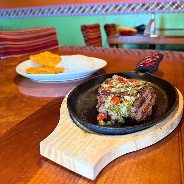 El Leoncito's sizzling steak with salsa, rice, and plantains on a wooden table.