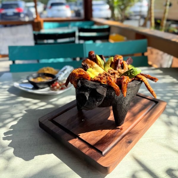 El Leoncito's molcajete overflowing with grilled meats, avocado, and lime, served on a wooden board.