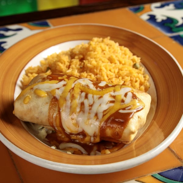 A large burrito covered in melted cheese and sauce, served with a side of yellow rice.