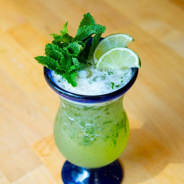 El Leoncito's vibrant green mojito cocktail, garnished with fresh mint and lime slices.