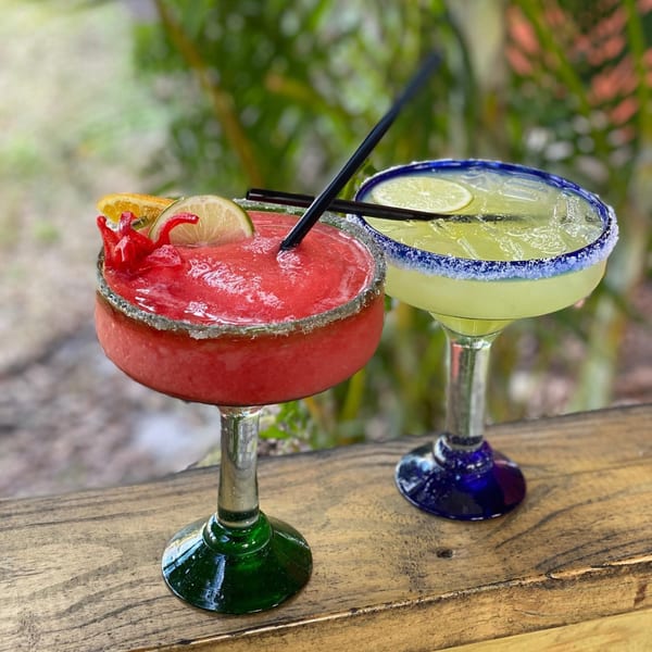 Two vibrant El Leoncito margaritas, one strawberry and one lime, on a rustic wooden surface.